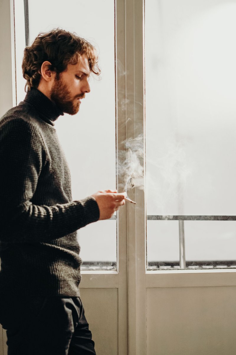 Man Wearing Black Sweater Standing Beside White Wooden Framed Glass Window While Smoking · Free Stock Photo