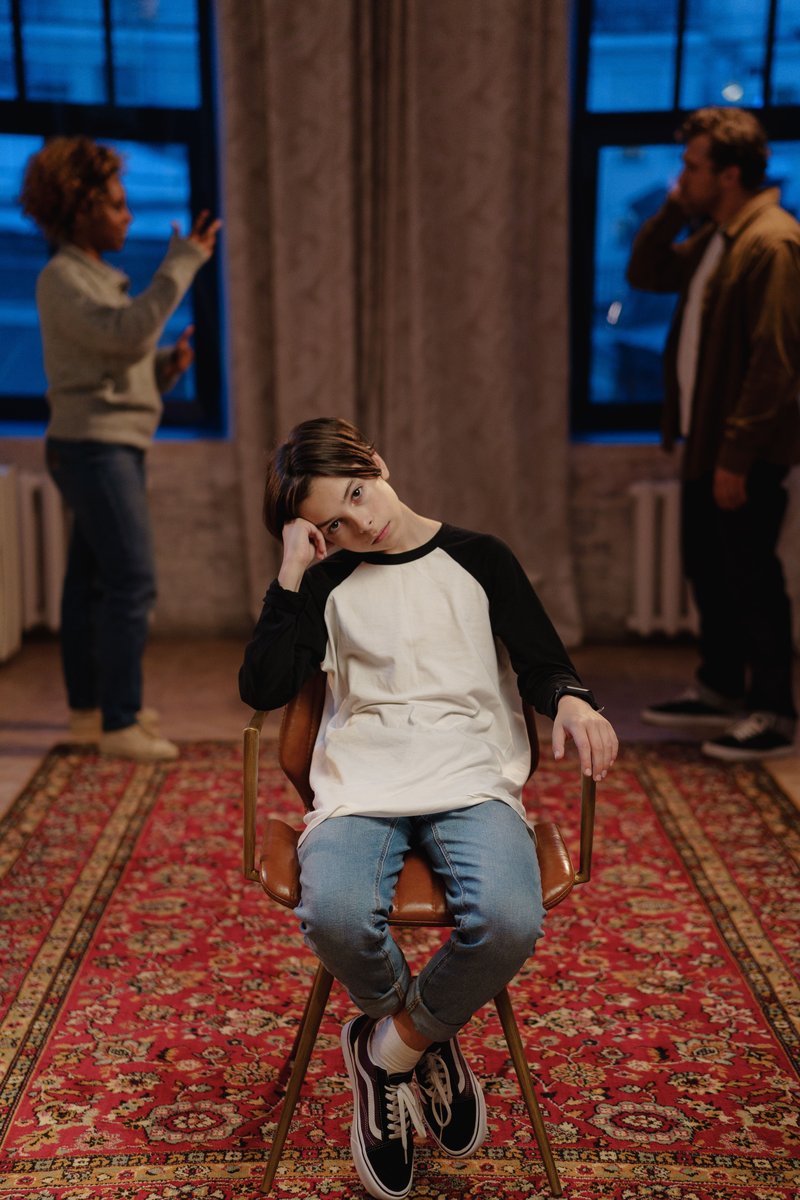 A Boy Sitting on a Chair with Quarreling Parents Behind ...