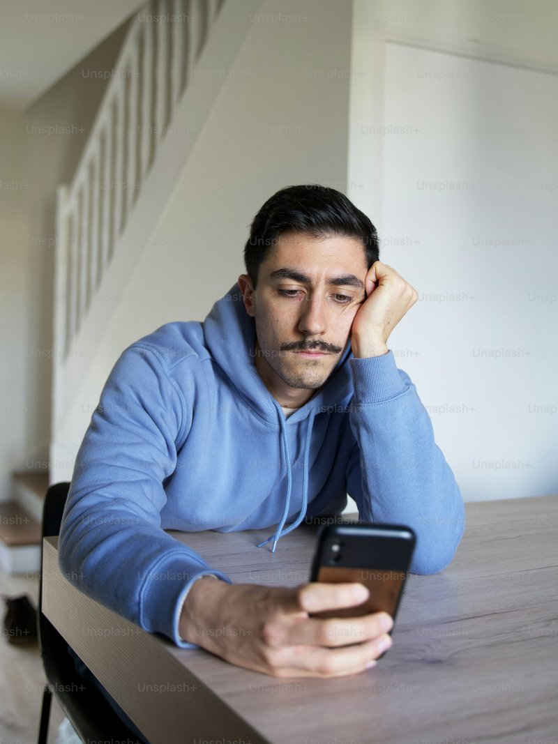 A man sitting at a table looking at a phone photo – Mental health Image on Unsplash