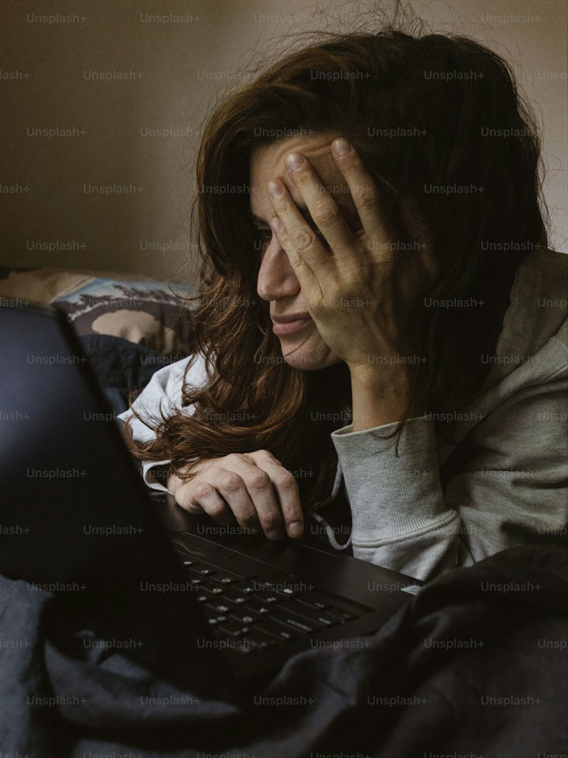 A woman covers her eyes while using a laptop photo – Sad ... A woman covers her eyes while using a laptop photo – Sad ...