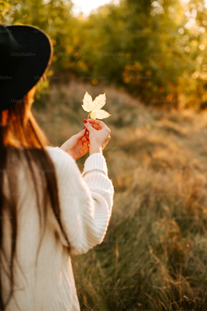 A woman in a black hat holding a leaf - Photo on Unsplash+