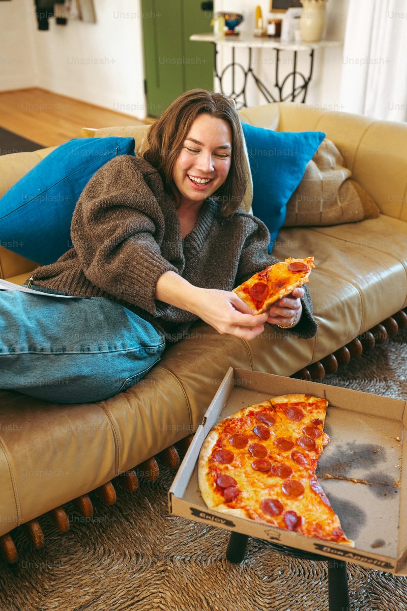 A woman sitting on a couch holding a slice of pizza - Photo ...