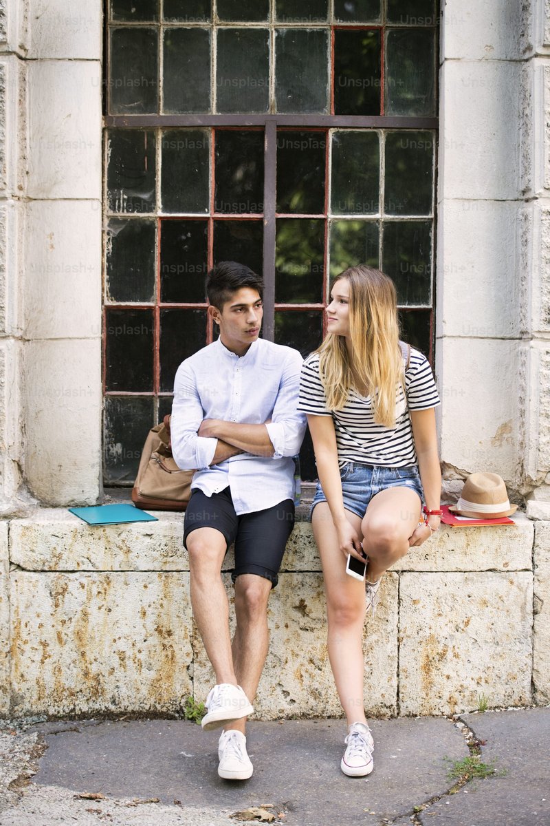 Attractive teenage student couple talking in front of university and sitting on stone bench - Photo on Unsplash+