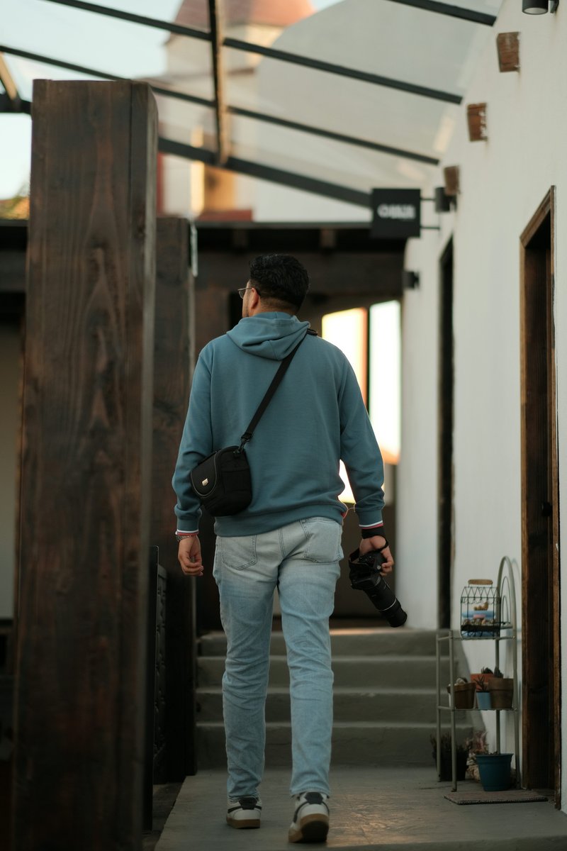 Man in hoodie walks away, holding a camera. photo – Free Photographer Image on Unsplash