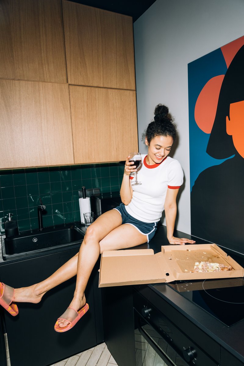 Young Woman Sitting on a Kitchen Counter While Looking at ... Young Woman Sitting on a Kitchen Counter While Looking at ...